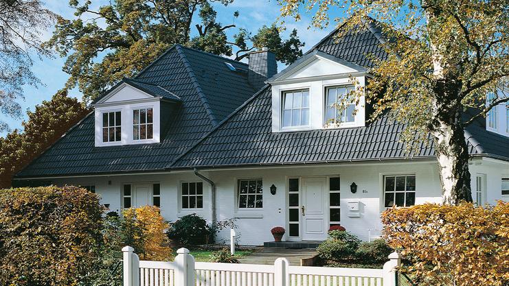 Elegantes zweigeschossiges Haus mit Satteldach, umgeben von Garten und weißem Zaun. Großer Eingangsbereich sichtbar.