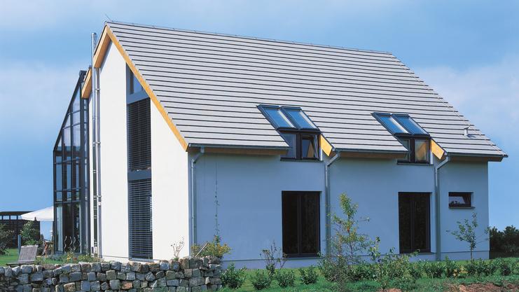 Moderne Doppelhaushälfte mit Satteldach und darunterliegenden Fenstern, umgeben von einem gepflegten Garten.